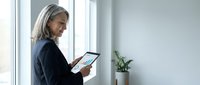 Mature businesswoman using digital tablet in modern office space with natural lighting and minimalist decor for professional workflow.