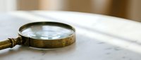 Vintage brass magnifying glass with wooden handle resting on white marble surface, suitable for antique, research, and detective themed projects.