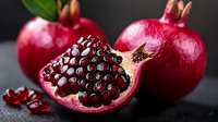 Ripe pomegranates with one cut open displaying red arils and seeds, isolated on dark background for food and culinary design use.