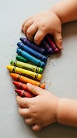 Child hands holding colorful wax crayons in rainbow arrangement for creative art projects and educational activities.