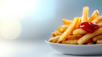 Golden crispy french fries served on white plate with red ketchup sauce, close-up view against blurred background. Fresh hot potato strips for fast food menu.