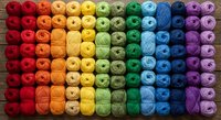 Colorful yarn balls arranged in rainbow gradient pattern for crafting and knitting projects on wooden background.