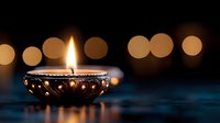 Traditional oil lamp with ornate metal design burning bright flame against warm bokeh lights background for Diwali festival celebration and spiritual meditation.