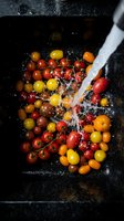 Fresh cherry tomatoes in red and yellow varieties being rinsed under running water on dark slate surface, ideal for food photography, cooking blogs, and culinary content.