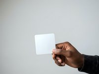 Male hand with dark skin tone holding blank white square card against neutral gray background, suitable for branding, marketing mockups, and promotional campaigns.