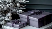 Elegant purple gift boxes with glittering ribbons next to snow-covered Christmas tree branches with silver ornaments, creating luxurious holiday atmosphere.
