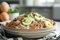 Fresh quinoa salad with hard boiled eggs, cherry tomatoes and herbs in white bowl on kitchen counter for healthy meal preparation and clean eating.