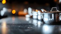 Stainless steel cooking pot on dark granite countertop with soft bokeh lights in background, modern kitchen atmosphere with selective focus and reflections.