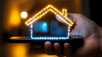 Glowing house silhouette made of sparkles floating above smartphone in dark room, concept of smart home technology and digital real estate solutions.