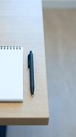Spiral-bound notebook with blank pages and dark blue ballpoint pen resting on wooden desk surface, suitable for business, education, writing, planning, and office workspace concepts.