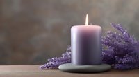 Glowing purple aromatherapy candle on stone holder with fresh lavender sprigs creating peaceful spa atmosphere against dark background. Wellness concept.