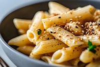 Creamy penne pasta with black pepper and herbs served on dark plate, close-up view of traditional Italian cuisine garnished with fresh parsley.