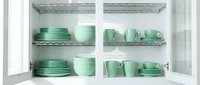 Mint green ceramic dinnerware set neatly arranged on white kitchen cabinet shelves, including plates, bowls, and cups in soft pastel tones.