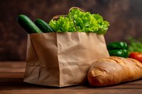 Fresh organic vegetables and bread in brown paper bag on wooden table for healthy grocery shopping and sustainable living.