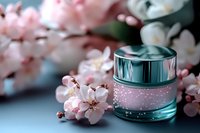 Luxury cosmetic cream jar with spring cherry blossom flowers on blue background, soft focus skincare product photography for beauty and wellness marketing.