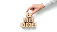 Hand placing wooden blocks with environmental icons in pyramid formation on white background for eco-friendly business concepts and sustainability planning.