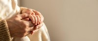 Elderly woman hands clasped together in prayer or meditation pose wearing cozy knit sweater. Peaceful moment of reflection and spirituality in soft natural light.