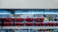 Fresh red strawberries displayed in plastic containers on grocery store shelves under bright LED lighting for retail sale and healthy eating choices.