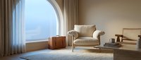 Elegant modern living room with arched window, beige armchair, vintage leather suitcase, and coastal view for interior design and home decor projects.