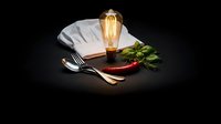 Elegant restaurant table setting with vintage Edison bulb lamp, white napkin, silverware and fresh herbs on dark background for fine dining establishments.