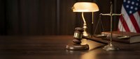 Wooden gavel and scales of justice on desk with warm lamp lighting in courtroom setting for legal proceedings and judicial decisions.