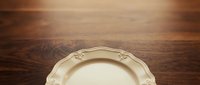 Vintage cream-colored decorative plate with ornate rim on rustic wooden surface, suitable for tableware, dining, and home decor design projects.