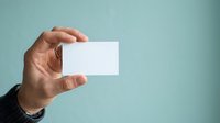 Close-up of male hand holding blank white business card against soft blue background, ready for branding and corporate identity design.