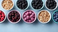 Fresh berries and granola in colorful ceramic bowls on blue background. Healthy breakfast ingredients with raspberries, blackberries, blueberries and muesli.