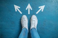 White sneakers and jeans standing at crossroads with three white arrows pointing in different directions on blue concrete floor, choice concept.