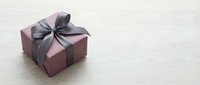 Elegant burgundy gift box with gray satin ribbon bow on light wooden surface for special occasions, holidays, birthdays, anniversaries and celebrations.