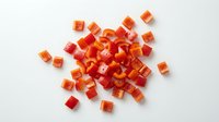 Small diced red bell pepper pieces scattered on white background, fresh chopped vegetable ingredient for cooking and meal preparation isolated.