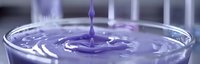 Purple liquid droplet creating ripple effect in glass container with smooth surface, captured in macro photography showing fluid dynamics and surface tension.
