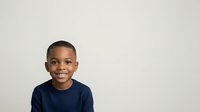 Young African American boy, approximately 6-8 years old, wearing a dark navy blue t-shirt, smiling at camera against neutral white background. Studio portrait suitable for educational, family, and commercial use.