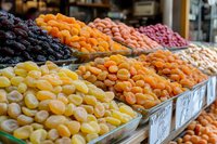Colorful assortment of dried fruits displayed in market bins, including apricots, dates, raisins, and figs arranged in neat rows for retail sale.
