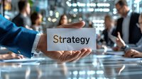 Business professional holding strategy card in modern office meeting with diverse team discussing plans in background, corporate planning concept.