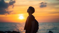 Young Asian male silhouette with backpack gazing at dramatic orange sunset over ocean horizon, capturing moment of peaceful solitude and wanderlust against vibrant sky.