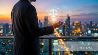 Businessman holding glowing scales of justice hologram against illuminated city skyline at dusk, symbolizing law, legal technology, and corporate justice.