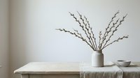 Minimalist spring home decor with pussy willow branches in ceramic vase on wooden table against neutral wall for seasonal interior design styling.