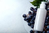 White cosmetic bottle with fresh dark grapes and water drops on light background for natural skincare and beauty product packaging design.