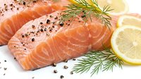 Fresh salmon fillet with dill herbs and lemon slices seasoned with black pepper on white background ready for cooking healthy seafood meal preparation.