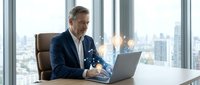 Middle-aged Caucasian businessman in suit working on laptop with glowing digital light bulb hologram, innovation and technology concept in modern office.