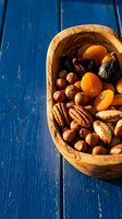Wooden bowl filled with mixed nuts and dried fruits on rustic blue wooden background for healthy snacking and cooking ingredients.