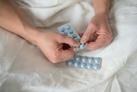 Male hands holding blue pills in blister pack on white bedding for healthcare and medication management concepts.