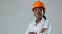 Young African American female construction engineer or architect wearing orange hard hat and white shirt poses with confident smile and crossed arms.