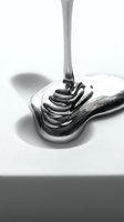Liquid metal pouring onto spoon in monochrome, creating flowing waves and reflective surfaces for abstract design and commercial use.