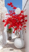 Vibrant red bougainvillea flowers cascade over white Mediterranean alley with paper lanterns, creating dramatic contrast against whitewashed walls and blue sky.