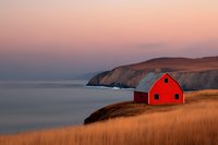 Red barn on coastal cliff overlooking tranquil ocean at sunset, dramatic landscape with golden grass and rocky shoreline in soft evening light.