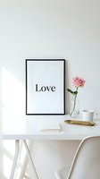 Minimalist white desk styled with a framed love print, pink rose in glass vase, gold tray, and coffee mug for home decor inspiration.