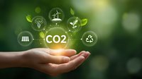 Hand holding glowing CO2 symbol with sustainable energy icons floating above against green natural background. Environmental conservation concept.
