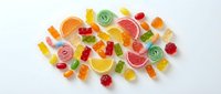 Colorful assorted gummy candies, jelly bears, fruit slices and swirl lollipops scattered on white background, isolated for design use.